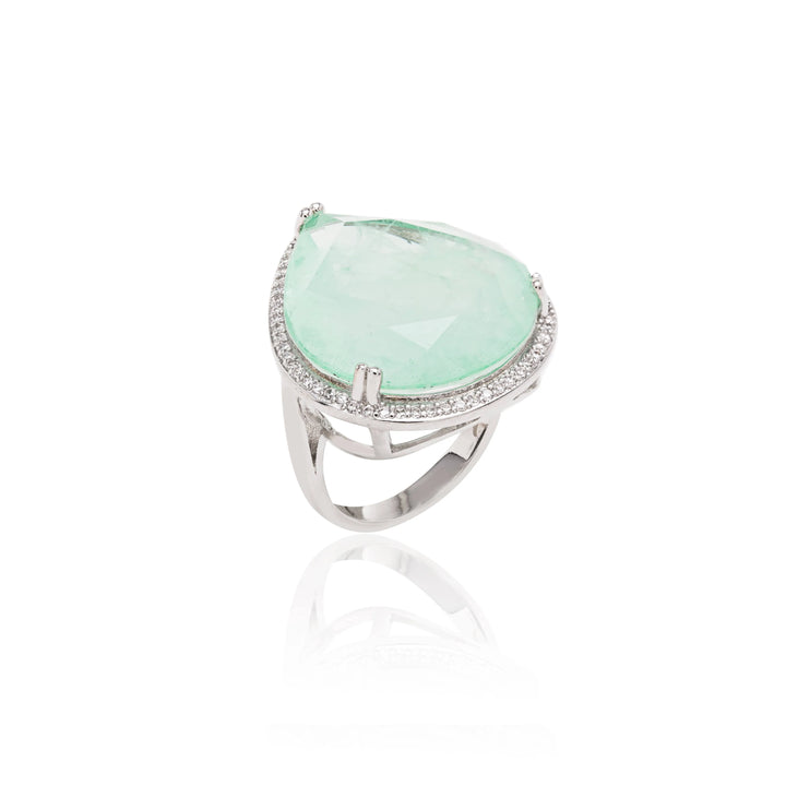 A rhodium-plated ring with a green Colombian emerald in the center and smaller clear crystals around it.