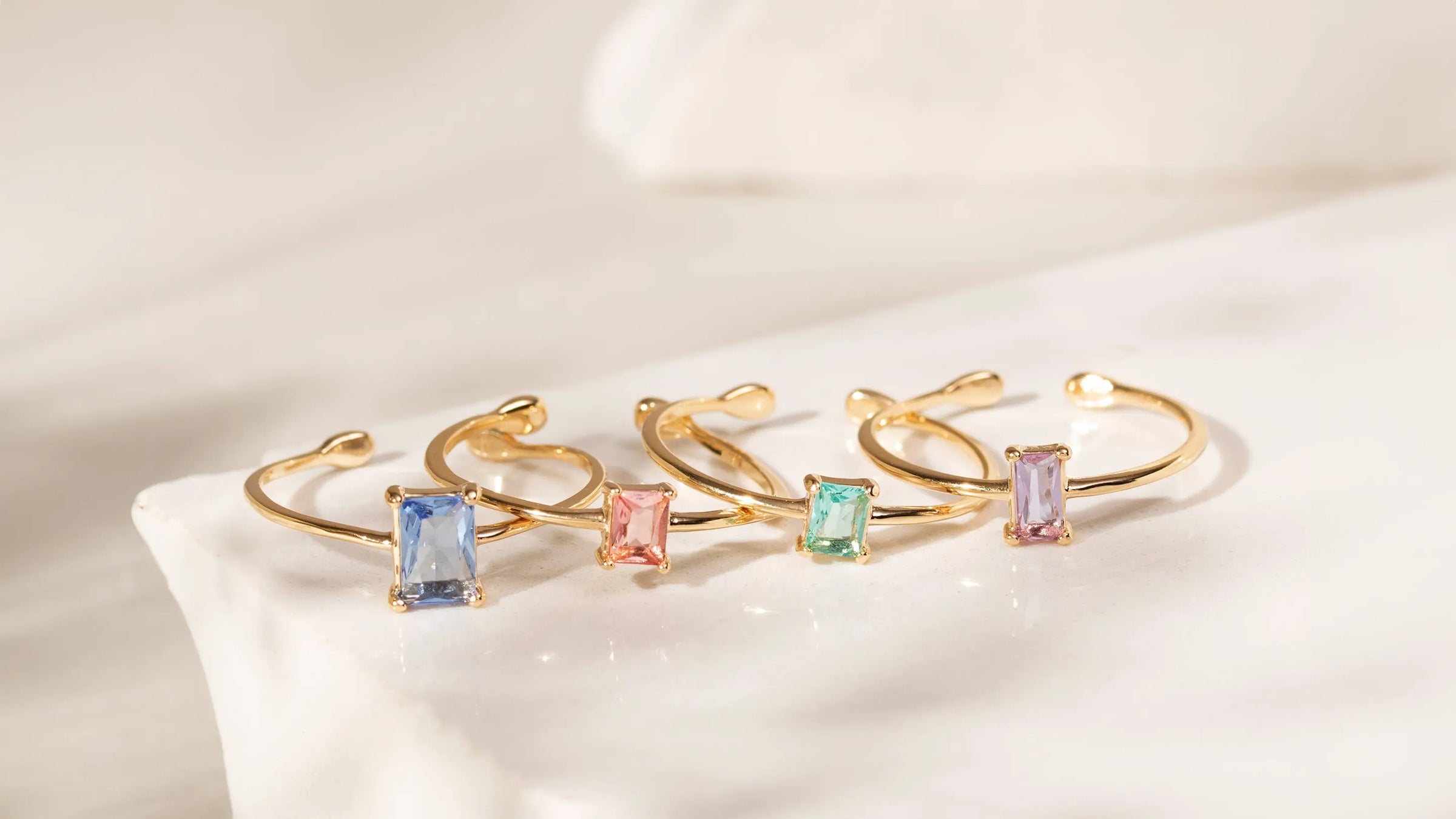 Assorted gold-plated rings with multicolored fusion stones set on a pristine white background, showcasing Elladora’s Best Sellers Collection.