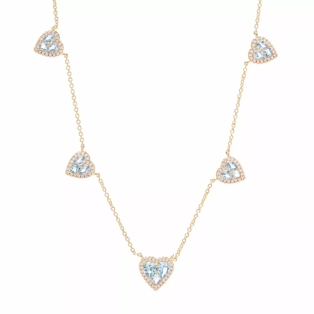 A delicate gold chain necklace featuring five heart-shaped clusters of clear pavé stones, with the center heart containing a light blue gemstone. The necklace is displayed on a clean white background.