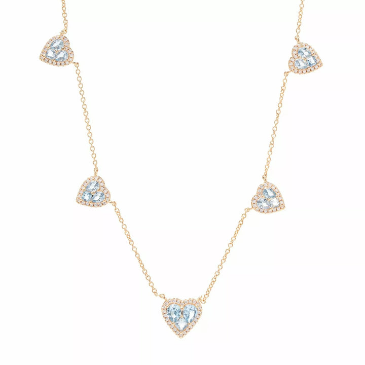 A delicate gold chain necklace featuring five heart-shaped clusters of clear pavé stones, with the center heart containing a light blue gemstone. The necklace is displayed on a clean white background.