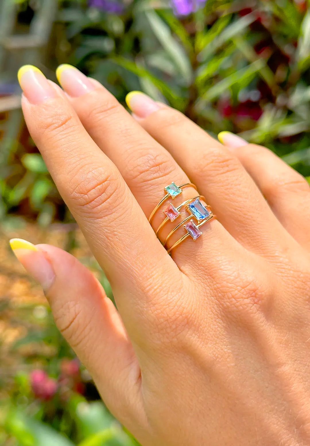 Close-up of a woman's hand featuring Elladora's gold-plated rings with blue, pink, and aquamarine fusion stones, illustrating the vibrant variety in the Best Sellers Collection.