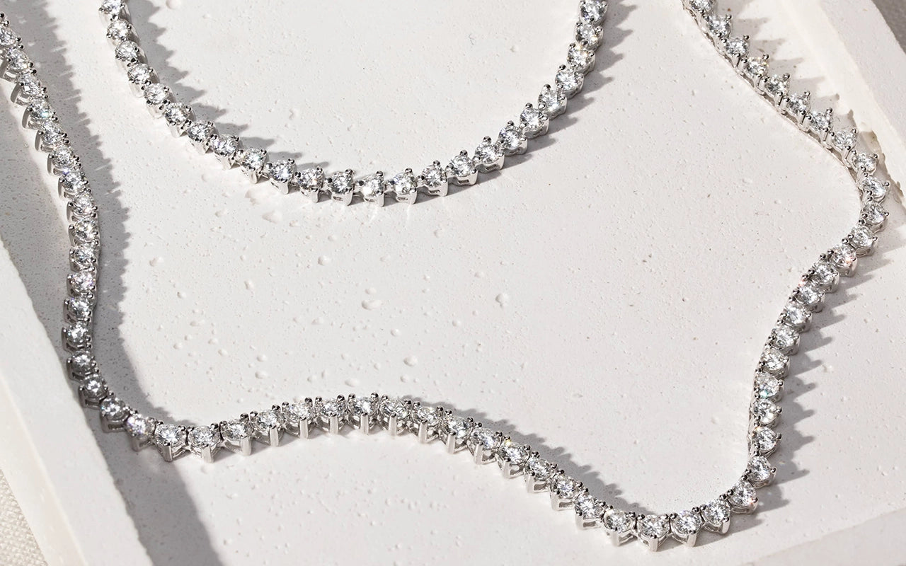Silver Moissanite Tennis necklace with clear stones on a textured white surface