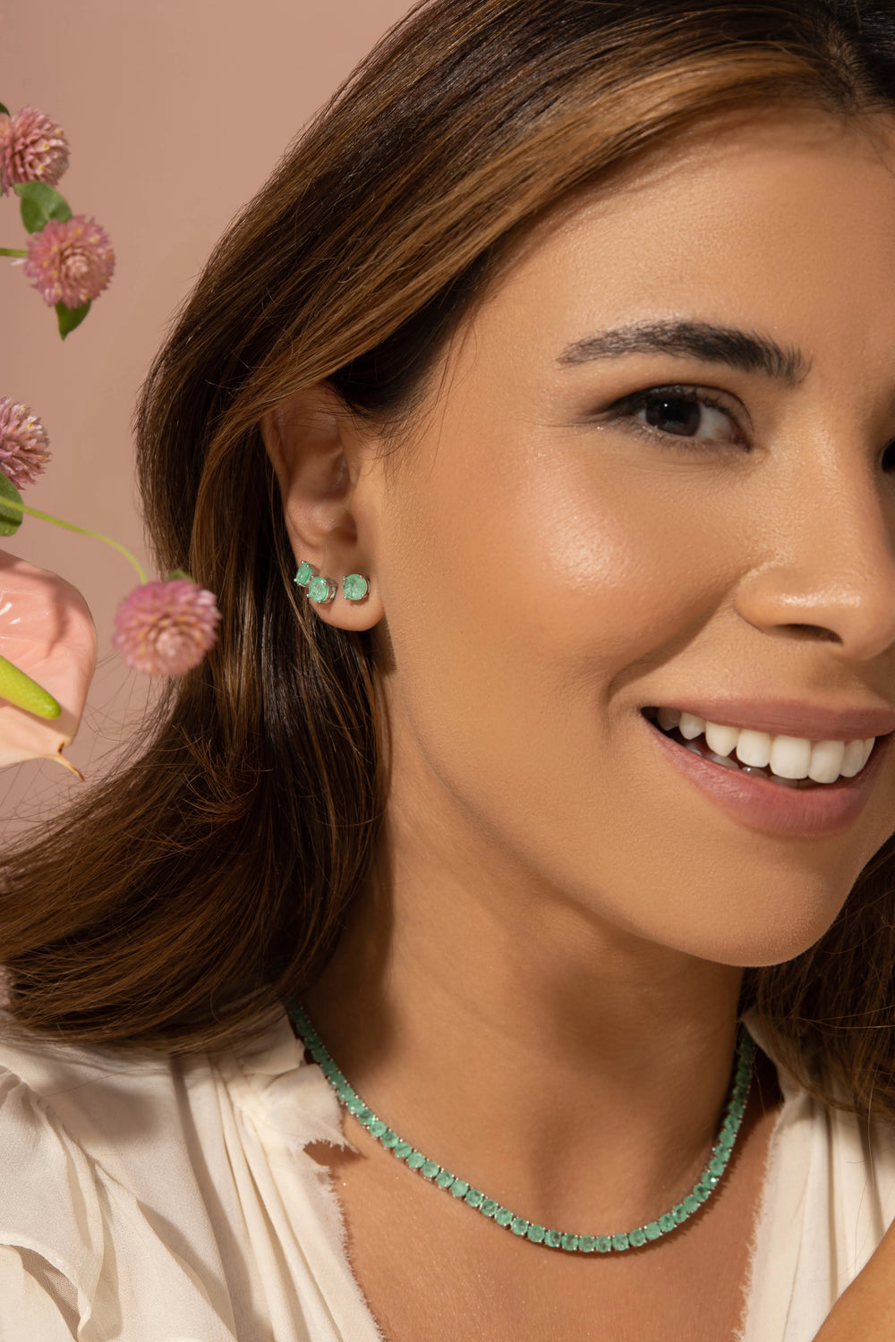 A woman wearing beautiful colombian emerald tennis necklace and studs in elegant pink pastel background