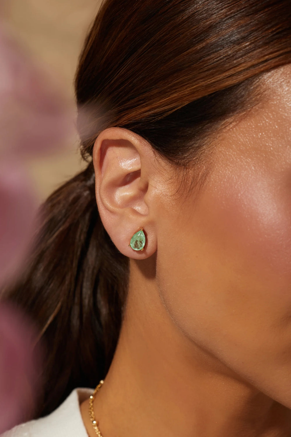 A close-up side profile of a woman wearing a small teardrop-shaped green gemstone stud earring in a silver setting.