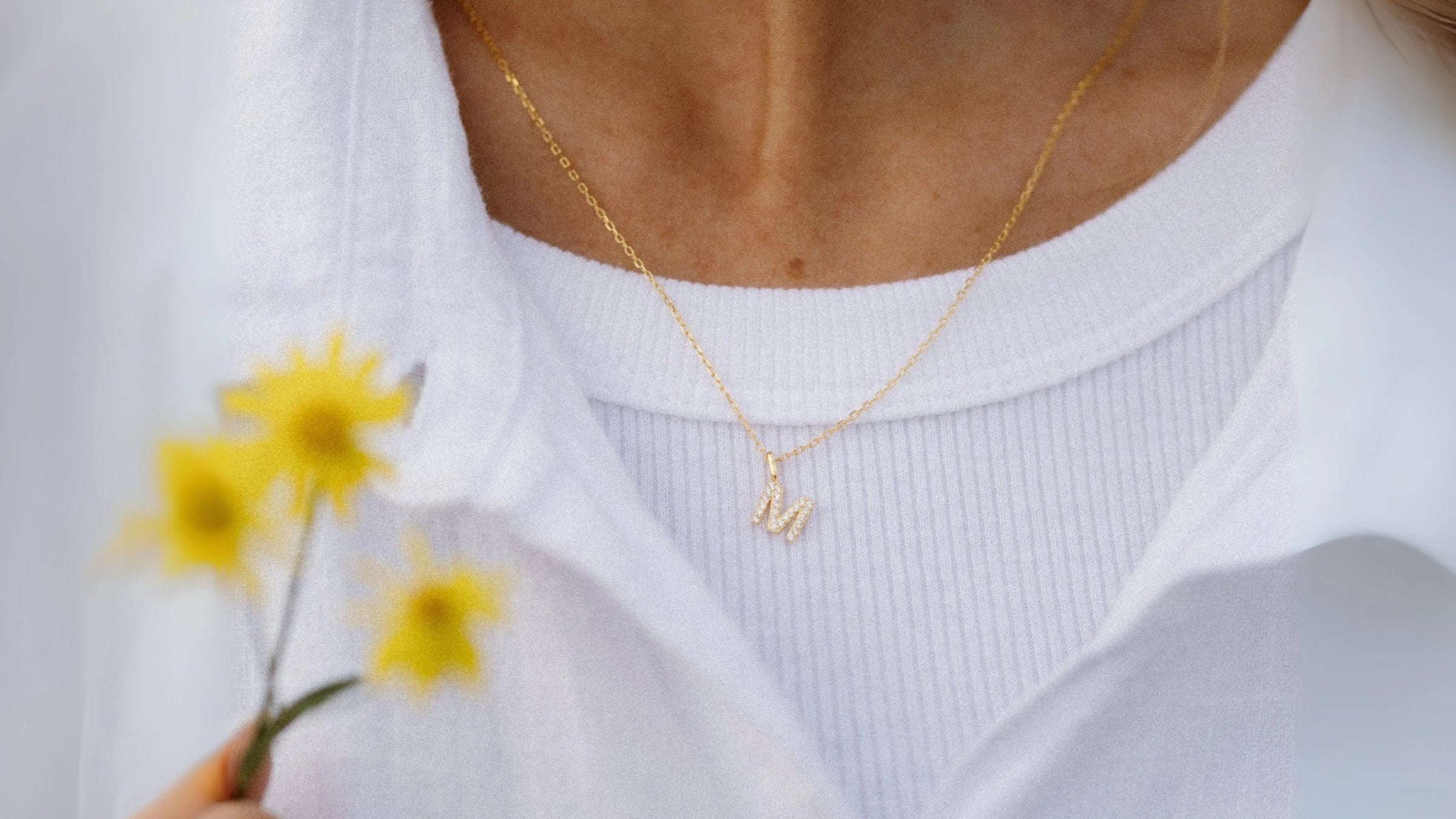 A woman wearing an 'M' initial necklace in a beautiful field of yellow flowers