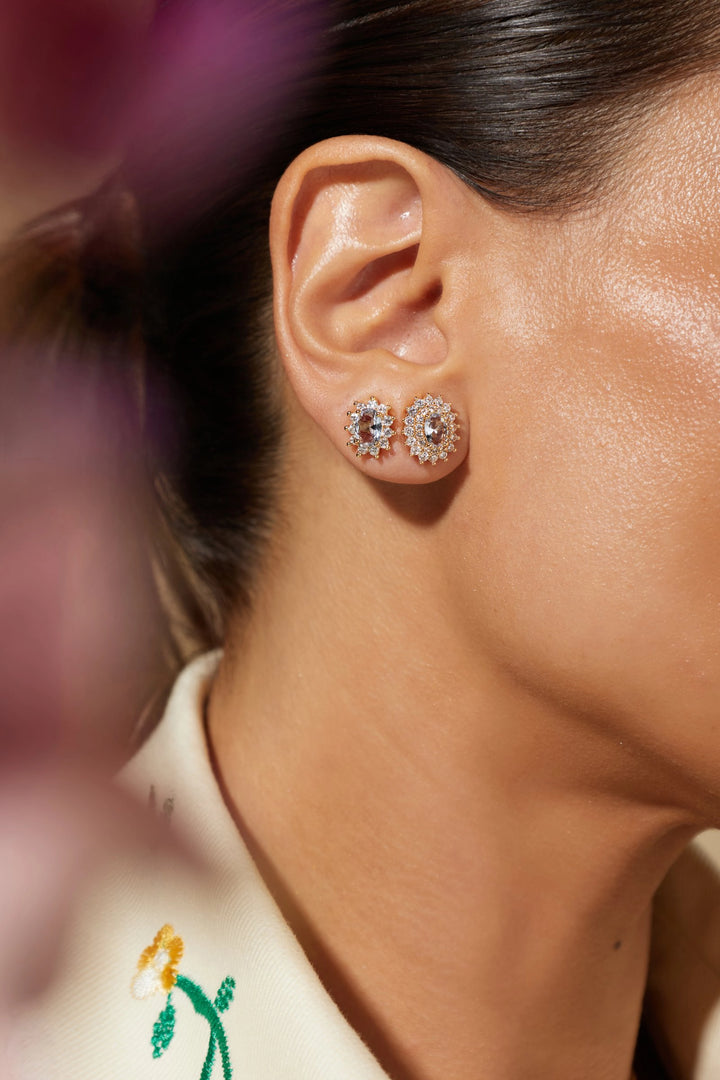 A close-up lifestyle shot of a model's ear wearing a pair of round, multi-layered silver-toned stud earrings with clear stones.