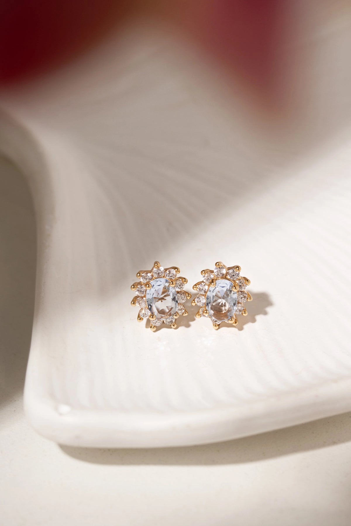 A pair of gold-toned stud earrings with oval clear gemstones, displayed on a white textured dish.