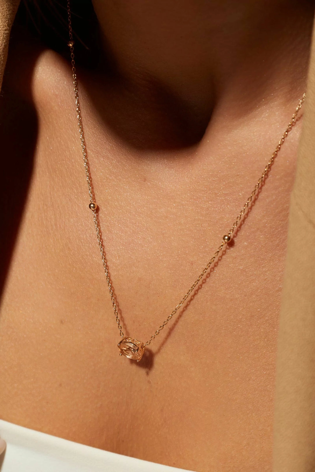 A close-up of a delicate rose gold chain necklace with small bead accents and a central geometric pendant, worn on a model's neck.
