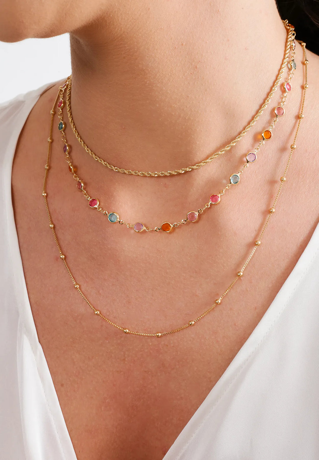 Elladora's signature gold necklaces adorned with multicolored fusion stones, draped elegantly on a white blouse for a touch of sophistication and vibrant style.