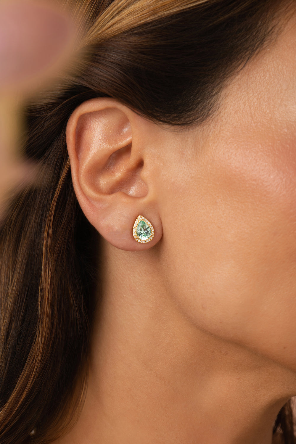 Close-up of an ear wearing a teardrop-shaped green gemstone earring.